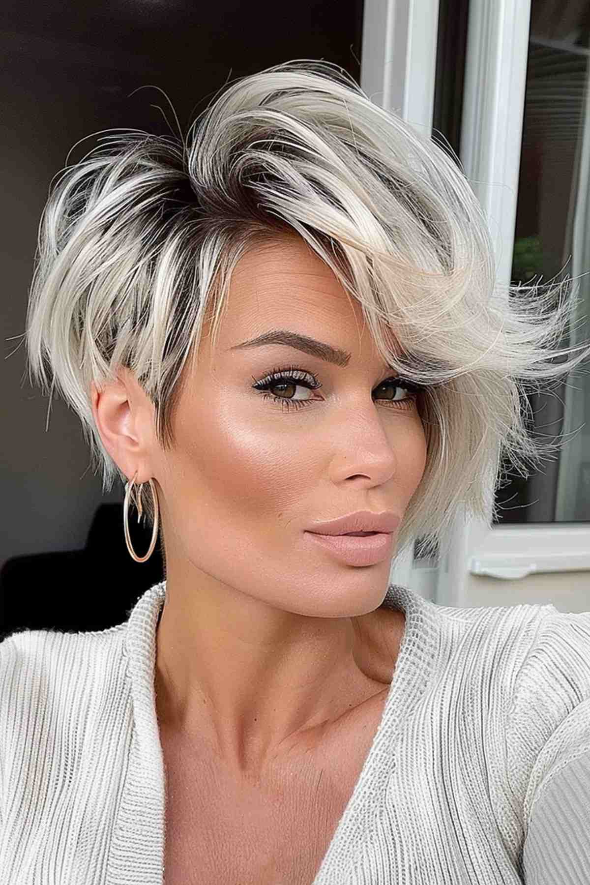 Asymmetrical platinum-highlighted pixie bob with dark roots for a low-maintenance yet trendy style.