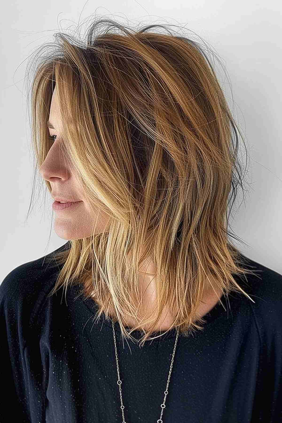 Profile view of a woman with a choppy layered long bob featuring dark to light hair color transition